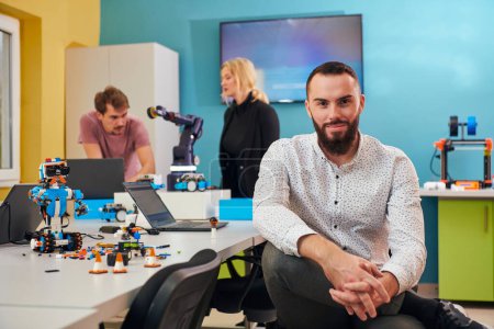 Foto de Un hombre sentado en un laboratorio de robótica mientras sus colegas en el fondo prueban nuevos inventos robóticos de vanguardia - Imagen libre de derechos