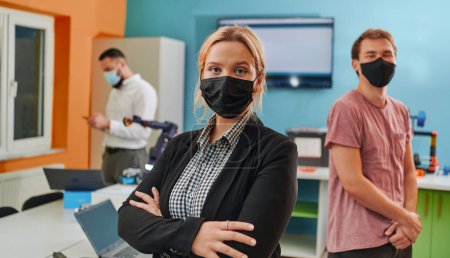 Photo for A woman wearing a protective mask standing in a laboratory while her colleagues test a new robotic invention in the background - Royalty Free Image