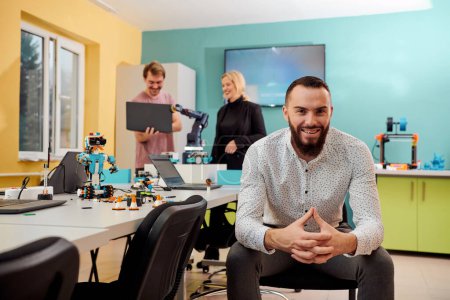 Téléchargez les photos : Un homme assis dans un laboratoire de robotique pendant que ses collègues testent en arrière-plan de nouvelles inventions robotiques de pointe - en image libre de droit