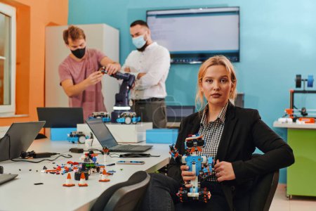 Téléchargez les photos : Une femme assise dans un laboratoire pour résoudre des problèmes et analyser la vérification des robots. En arrière-plan, des collègues prennent la parole lors d'une réunion en ligne. - en image libre de droit