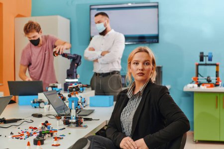Téléchargez les photos : Une femme assise dans un laboratoire pour résoudre des problèmes et analyser la vérification des robots. En arrière-plan, des collègues prennent la parole lors d'une réunion en ligne. - en image libre de droit