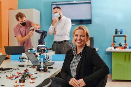 Foto de Una mujer sentada en un laboratorio mientras sus colegas prueban un nuevo invento robótico en el fondo. - Imagen libre de derechos