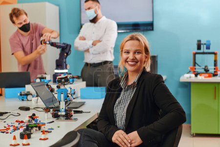 Photo for A woman sitting in a laboratory while her colleagues test a new robotic invention in the background. - Royalty Free Image
