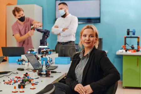 Foto de Una mujer sentada en un laboratorio mientras sus colegas prueban un nuevo invento robótico en el fondo. - Imagen libre de derechos