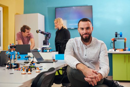 Foto de Un hombre sentado en un laboratorio de robótica mientras sus colegas en el fondo prueban nuevos inventos robóticos de vanguardia - Imagen libre de derechos