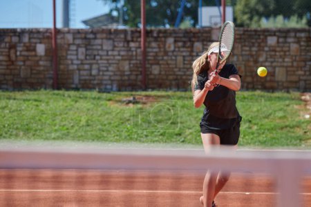 Téléchargez les photos : Une jeune fille montrant des compétences professionnelles de tennis dans un match de compétition par une journée ensoleillée, entouré par l'esthétique moderne d'un court de tennis - en image libre de droit