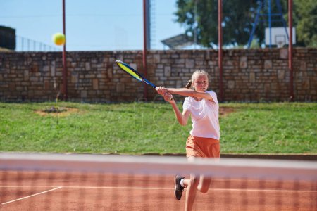 Photo for A young girl showing professional tennis skills in a competitive match on a sunny day, surrounded by the modern aesthetics of a tennis court - Royalty Free Image