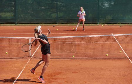 Foto de Chicas jóvenes en un animado partido de tenis en un día soleado, demostrando sus habilidades y entusiasmo en una pista de tenis moderna - Imagen libre de derechos