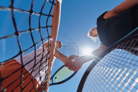 Foto de Dos jugadoras de tenis estrechando la mano con sonrisas en un día soleado, exudando deportividad y amistad después de un partido competitivo - Imagen libre de derechos