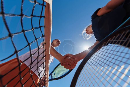 Foto de Dos jugadoras de tenis estrechando la mano con sonrisas en un día soleado, exudando deportividad y amistad después de un partido competitivo - Imagen libre de derechos