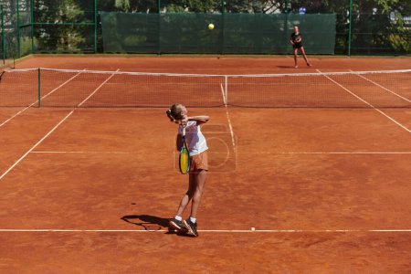 Foto de Chicas jóvenes en un animado partido de tenis en un día soleado, demostrando sus habilidades y entusiasmo en una pista de tenis moderna - Imagen libre de derechos