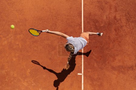 Top view of a professional female tennis player serves the tennis ball on the court with precision and power. 