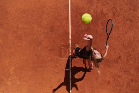 Top view of a professional female tennis player serves the tennis ball on the court with precision and power.