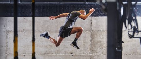 Téléchargez les photos : Un homme musclé capturé dans l'air alors qu'il saute dans un gymnase moderne, montrant son athlétisme, sa puissance et sa détermination à travers une routine de fitness de haute intensité. - en image libre de droit