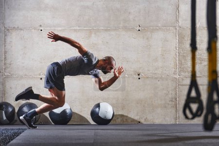 Foto de Un hombre musculoso capturado en el aire mientras salta en un gimnasio moderno, mostrando su atletismo, poder y determinación a través de una rutina de fitness de alta intensidad. - Imagen libre de derechos