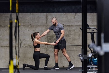 Photo for A muscular man assisting a fit woman in a modern gym as they engage in various body exercises and muscle stretches, showcasing their dedication to fitness and benefiting from teamwork and support. - Royalty Free Image