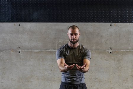 Téléchargez les photos : Un homme musclé travaillant des exercices d'étirement pour ses bras et les muscles du corps dans la salle de gym moderne . - en image libre de droit