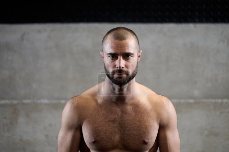 Photo for A muscular man poses in the gym, showcasing his strength and dedication to fitness through an impressive physique and glistening sweat on his face - Royalty Free Image