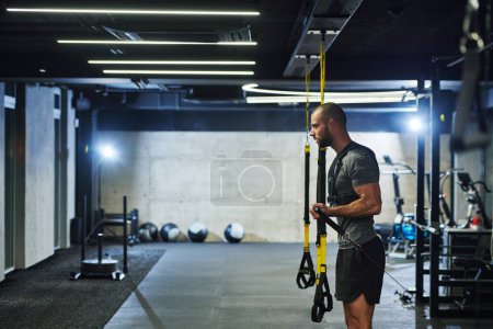 Foto de Un hombre musculoso en el gimnasio, preparándose para su entrenamiento, emana determinación y concentración a medida que se prepara para superar sus límites y lograr sus objetivos de fitness. - Imagen libre de derechos