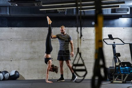 Téléchargez les photos : Un homme musclé aidant une femme en forme dans une salle de gym moderne alors qu'ils s'engagent dans divers exercices du corps et des étirements musculaires, montrant leur dévouement à la forme physique et bénéficiant du travail d'équipe et de soutien. - en image libre de droit