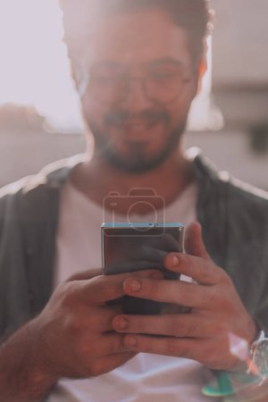 Photo for A young man utilizes his smartphone outdoors, showcasing the seamless integration of technology and mobility in modern professional life - Royalty Free Image