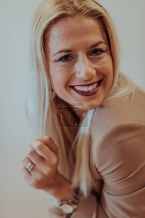 Foto de Una mujer de negocios segura y exitosa, con una amplia sonrisa, posa frente a un fondo beige, exudando profesionalidad y elegancia. - Imagen libre de derechos