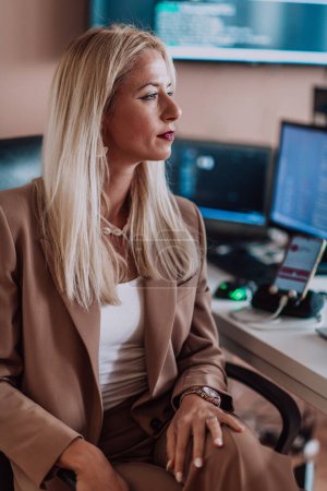Photo for A businesswoman sitting in a programmers office surrounded by computers, showing her expertise and dedication to technology - Royalty Free Image
