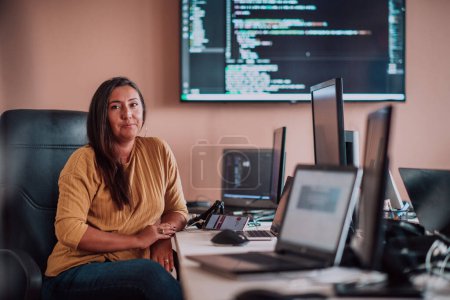 Téléchargez les photos : Une femme d'affaires assise dans un bureau de programmeurs entouré d'ordinateurs, montrant son expertise et son dévouement à la technologie - en image libre de droit