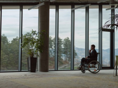 Téléchargez les photos : Un homme d'affaires mélancolique assis dans un fauteuil roulant avec une expression triste, regardant par la fenêtre d'un bureau moderne, transmettant un sentiment de solitude. - en image libre de droit