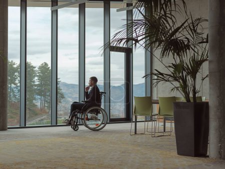 Téléchargez les photos : Un homme d'affaires mélancolique assis dans un fauteuil roulant avec une expression triste, regardant par la fenêtre d'un bureau moderne, transmettant un sentiment de solitude. - en image libre de droit