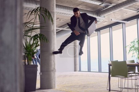 Foto de En la oficina moderna, un hombre de negocios con un maletín cautiva a todo el mundo mientras realiza emocionantes acrobacias aéreas, desafiando la gravedad con sus atrevidos saltos y mostrando su agilidad con impresionante - Imagen libre de derechos