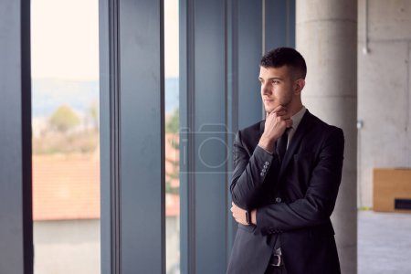 Foto de El hombre de negocios confiado en un traje elegante toma una pose, exudando carisma y profesionalismo, en medio del ambiente moderno de la oficina - Imagen libre de derechos