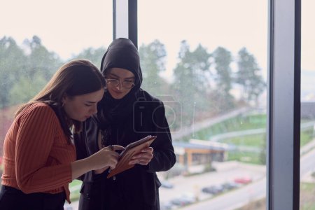 Foto de En una oficina moderna, un par de colegas, uno con un hijab, participan en una animada discusión, compartiendo sus ideas de negocio y fomentando un entorno de trabajo diverso e inclusivo. - Imagen libre de derechos