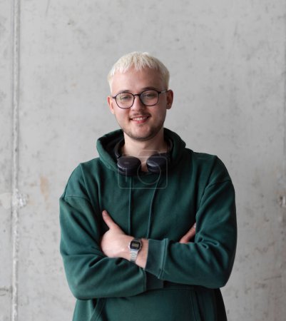 Photo for A man with blue hair, eyeglasses, and a green sweatshirt confidently poses with his arms crossed against a gray background, showcasing his fashionable and unique style - Royalty Free Image
