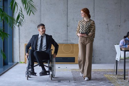 Foto de Un hombre de negocios en silla de ruedas y su compañera en una oficina moderna, representando el poder del trabajo en equipo, la inclusión y el apoyo, fomentando un ambiente de trabajo dinámico e inclusivo - Imagen libre de derechos