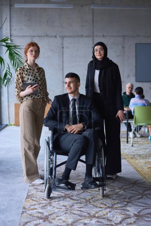 Foto de Un hombre de negocios con discapacidad en una silla de ruedas está rodeado de colegas de apoyo en una oficina moderna, mostrando la fuerza del trabajo en equipo, la inclusión y el empoderamiento frente a los desafíos - Imagen libre de derechos