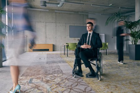 Téléchargez les photos : Un homme d'affaires en fauteuil roulant dans un bureau moderne, entouré de ses collègues qui sont représentés avec des mouvements flous, symbolisant leur soutien et leur solidarité alors qu'ils naviguent dans l'espace de travail - en image libre de droit