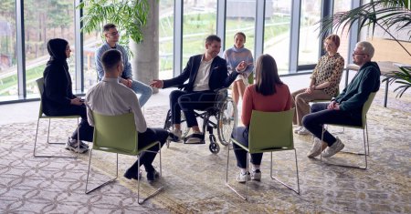 Téléchargez les photos : Un homme d'affaires en fauteuil roulant au centre du cercle, partageant passionnément ses idées d'affaires avec ses collègues, favorisant une atmosphère de collaboration et d'innovation dans une dynamique et - en image libre de droit