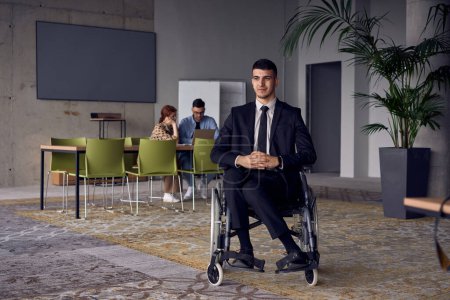 Photo for Businessman in a wheelchair commands attention, symbolizing resilience and success amidst a dynamic modern office environment - Royalty Free Image
