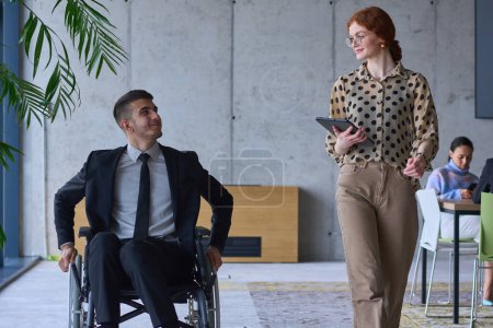 Foto de Un hombre de negocios en silla de ruedas y su compañera en una oficina moderna, representando el poder del trabajo en equipo, la inclusión y el apoyo, fomentando un ambiente de trabajo dinámico e inclusivo - Imagen libre de derechos
