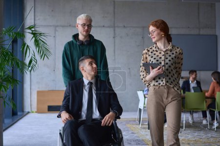 Photo for A group of business colleagues in a modern office exemplifies inclusivity and support as they compassionately wheel their business friend in a wheelchair, showcasing teamwork and empowerment in the - Royalty Free Image