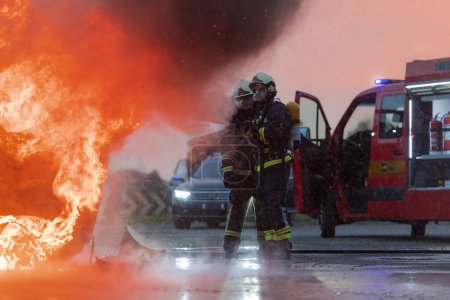 Téléchargez les photos : Les pompiers qui utilisent un extincteur à eau pour combattre la flamme dans un accident de voiture. Sauvetage du concept de sécurité industrielle et publique pendant la nuit. Photo de haute qualité - en image libre de droit