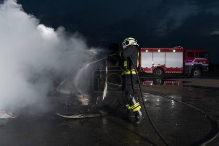 Téléchargez les photos : Les pompiers qui utilisent un extincteur à eau pour combattre la flamme dans un accident de voiture. Sauvetage du concept de sécurité industrielle et publique pendant la nuit. Photo de haute qualité - en image libre de droit