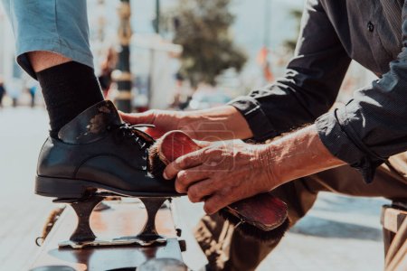 Téléchargez les photos : Un vieil homme polissant à la main et peignant une chaussure noire dans la rue. - en image libre de droit
