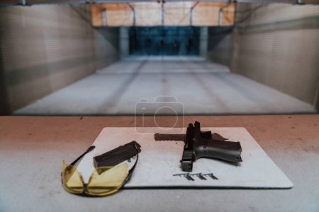 Foto de Equipo de tiro delante del objetivo. Pistola, gafas y auriculares en la mesa de un moderno campo de tiro. - Imagen libre de derechos