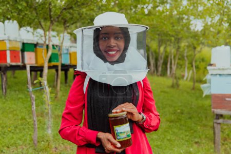 Photo for Portrait of a Muslim African American woman in the beekeeping department of a honey farm holding a jar of honey in her hand. - Royalty Free Image