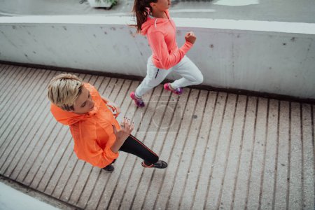 Photo for Two women in sports clothes running in a modern urban environment. The concept of a sporty and healthy lifestyle. - Royalty Free Image