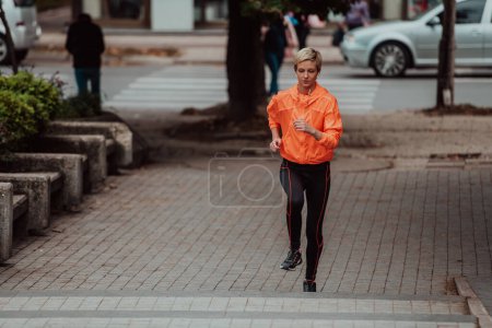 Téléchargez les photos : Une blonde en tenue de sport court autour de la ville dans un environnement urbain. La blonde chaude maintient un mode de vie sain - en image libre de droit