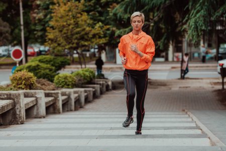 Foto de A blonde in a sports outfit is running around the city in an urban environment. The hot blonde maintains a healthy lifestyle - Imagen libre de derechos