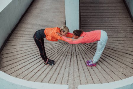 Téléchargez les photos : Two women warming up together and preparing for a morning run in an urban environment. Selective focus . - en image libre de droit